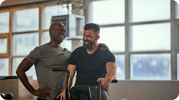 Dois homens em roupas de ginástica sorrindo juntos em uma academia.